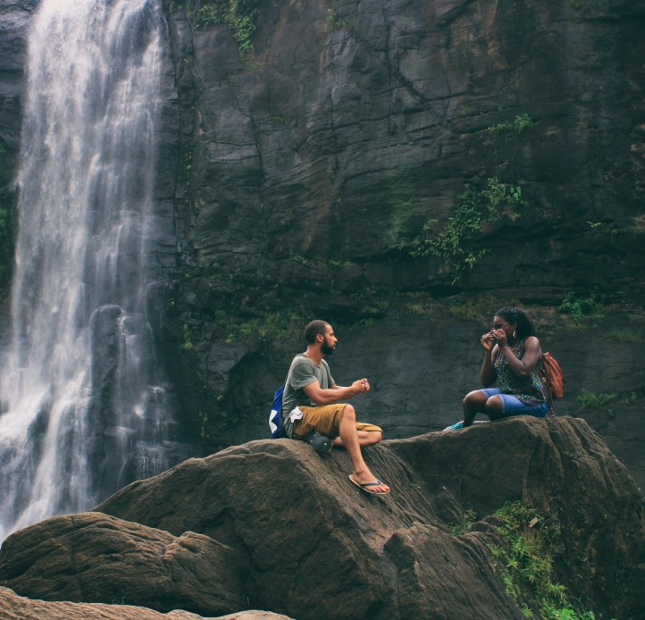 man and woman sitting in front of waterfall